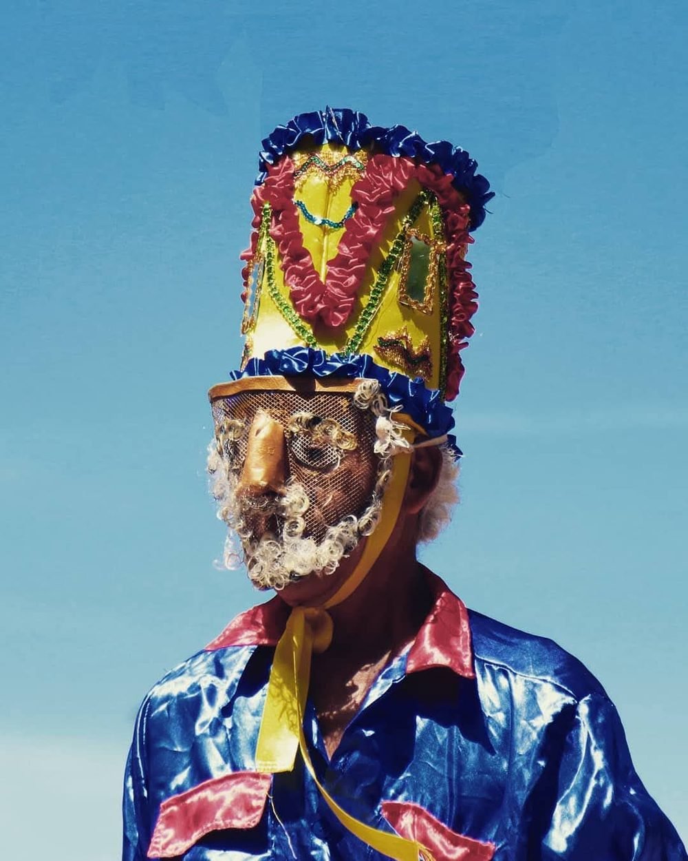 Personaje del sainete con máscara y gorro adornado contra el cielo