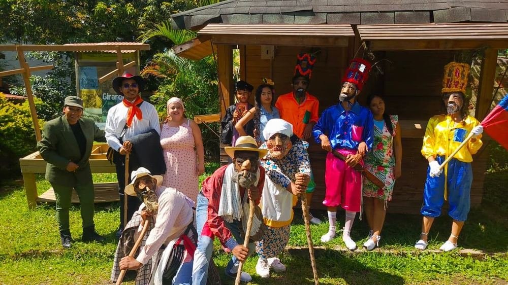 Grupo completo del sainete con vestuario y máscaras frente a una casa de madera